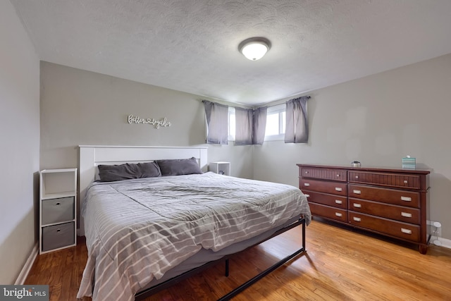 bedroom featuring a textured ceiling, light wood finished floors, and baseboards