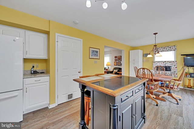 kitchen with light stone counters, light wood-style floors, freestanding refrigerator, white cabinetry, and decorative light fixtures