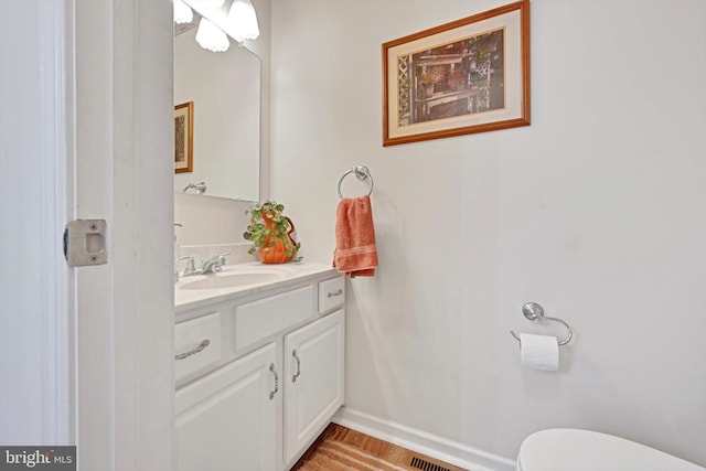 half bathroom featuring baseboards, wood finished floors, toilet, and vanity