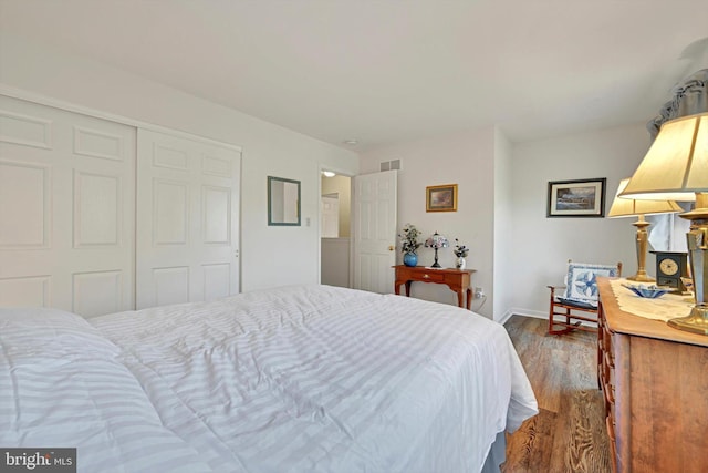 bedroom with baseboards, visible vents, wood finished floors, and a closet