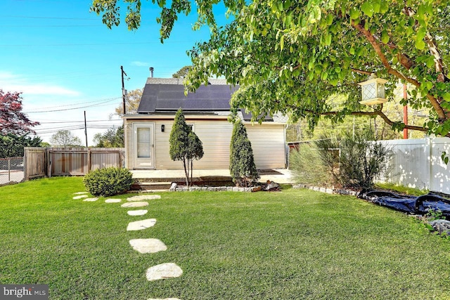 rear view of property featuring a fenced backyard, a yard, and solar panels