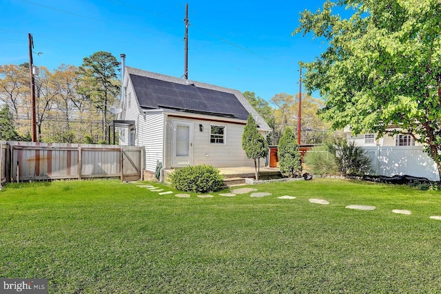 rear view of property with roof mounted solar panels, a wooden deck, a lawn, and a fenced backyard