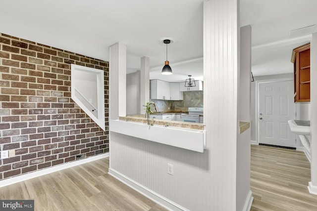 kitchen with light wood-style floors, decorative backsplash, brick wall, and electric stove