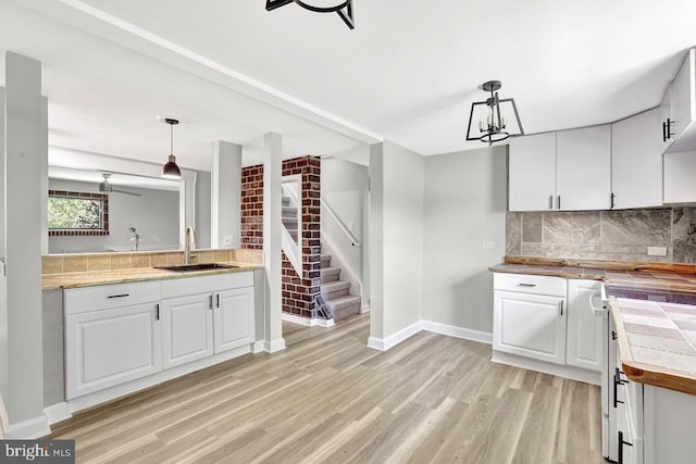 kitchen with white cabinets, tasteful backsplash, a sink, light wood finished floors, and decorative light fixtures
