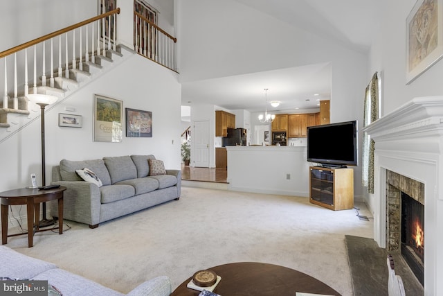 living area featuring a fireplace with flush hearth, stairs, a towering ceiling, and light carpet