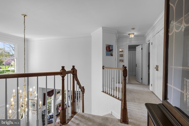 hall with carpet floors, ornamental molding, an upstairs landing, and an inviting chandelier