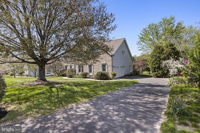 view of front facade featuring an attached garage, a front lawn, brick siding, and aphalt driveway