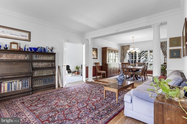 living area with ornate columns, an inviting chandelier, ornamental molding, and wood finished floors