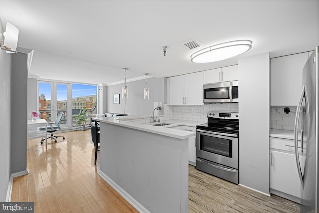 kitchen with a peninsula, white cabinetry, tasteful backsplash, a sink, and appliances with stainless steel finishes