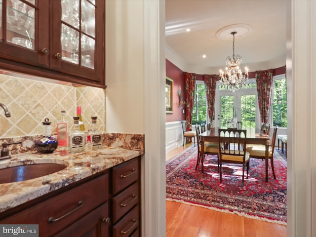 dining room featuring crown molding, wainscoting, wood finished floors, bar, and a chandelier