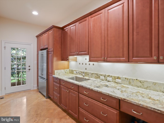 kitchen with freestanding refrigerator, recessed lighting, brown cabinets, light stone counters, and a sink