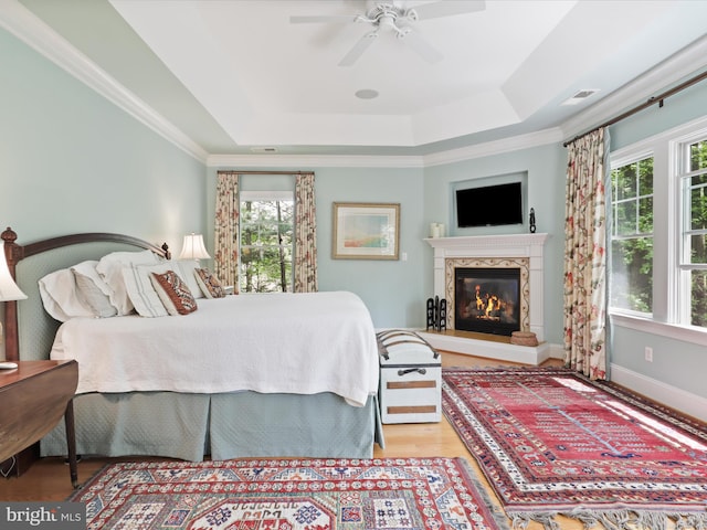 bedroom featuring a high end fireplace, a raised ceiling, multiple windows, and wood finished floors