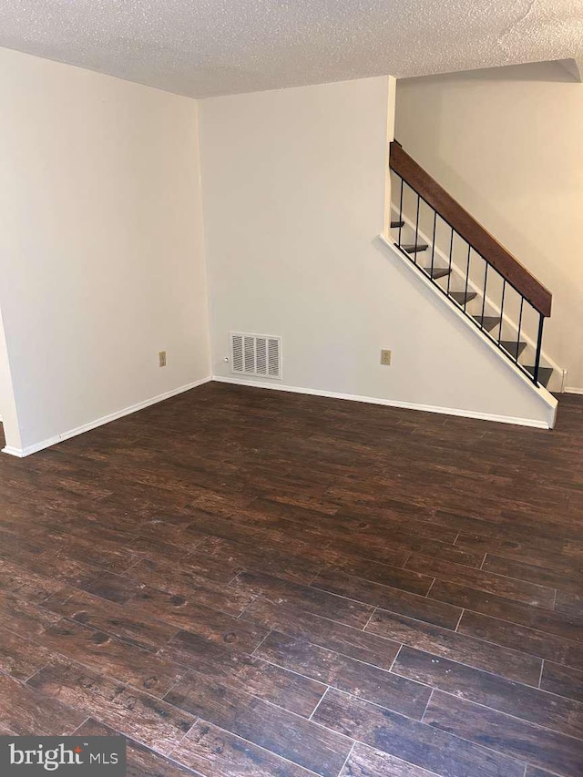 unfurnished living room with wood finished floors, stairway, baseboards, visible vents, and a textured ceiling