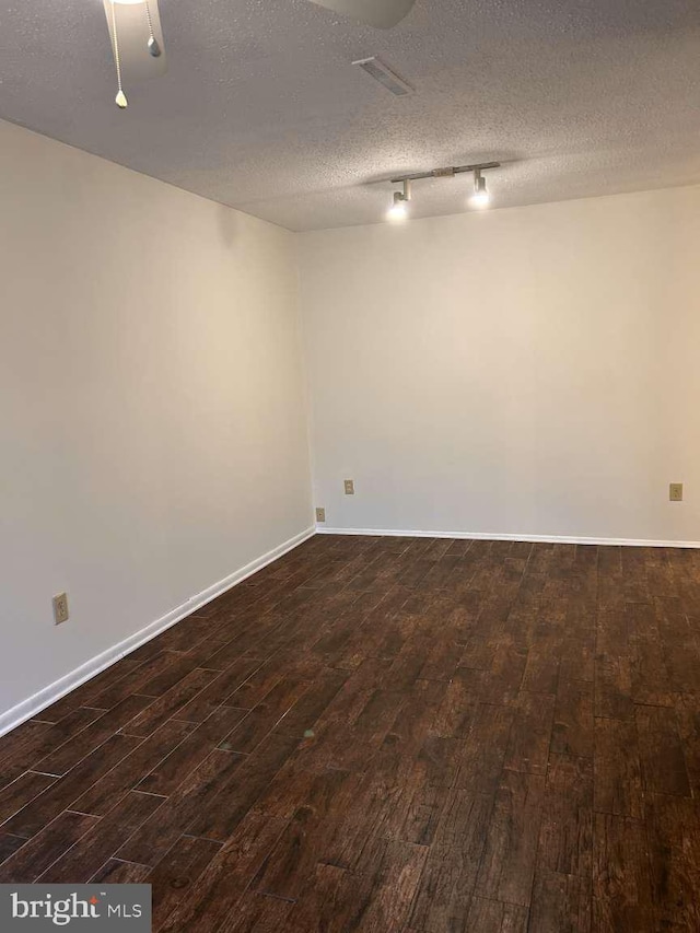 unfurnished room with rail lighting, a textured ceiling, visible vents, and dark wood-style floors