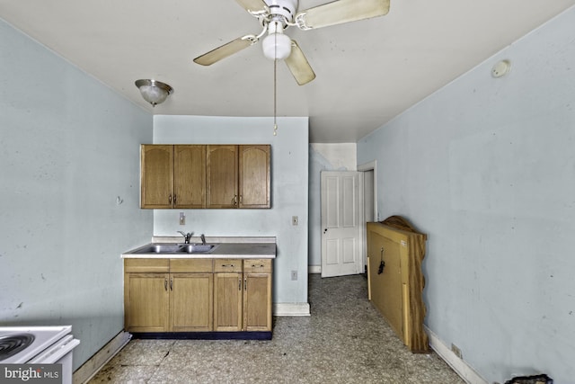 kitchen with baseboards, ceiling fan, brown cabinetry, and a sink