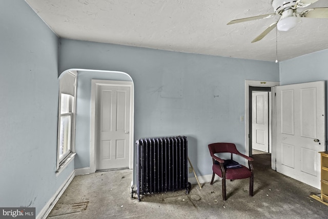 living area with a ceiling fan, baseboards, radiator, and a textured ceiling