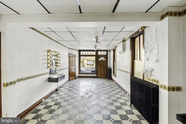 interior space with baseboards, radiator, tile patterned floors, and a drop ceiling