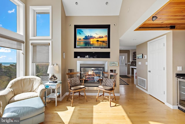 living area with a high ceiling, a multi sided fireplace, baseboards, light wood-type flooring, and visible vents