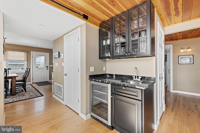 bar featuring wine cooler, light wood-style floors, baseboards, indoor wet bar, and a sink