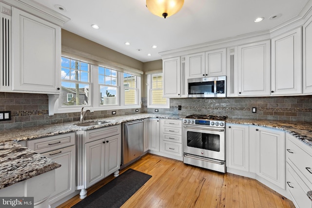 kitchen with backsplash, appliances with stainless steel finishes, a sink, white cabinets, and light wood-style flooring