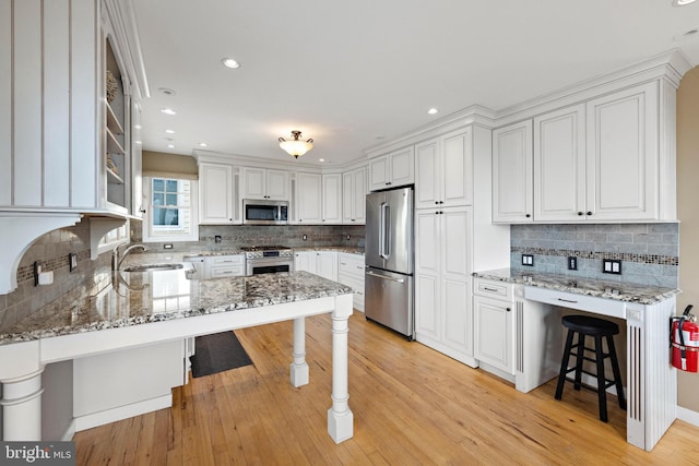kitchen featuring appliances with stainless steel finishes, white cabinets, backsplash, and a kitchen bar
