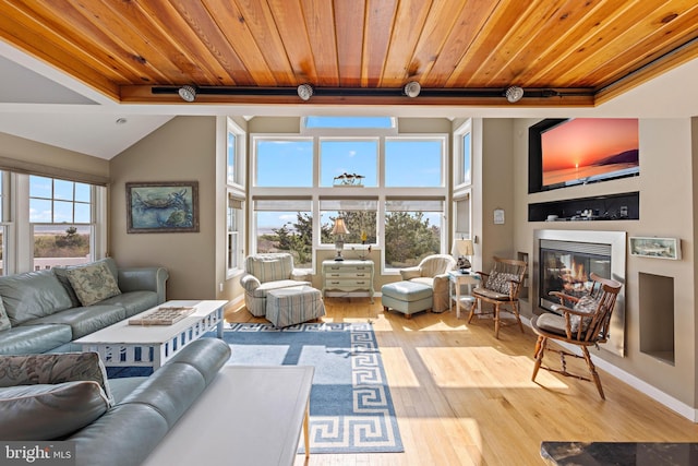 living room with lofted ceiling with beams, wood ceiling, a glass covered fireplace, and wood finished floors
