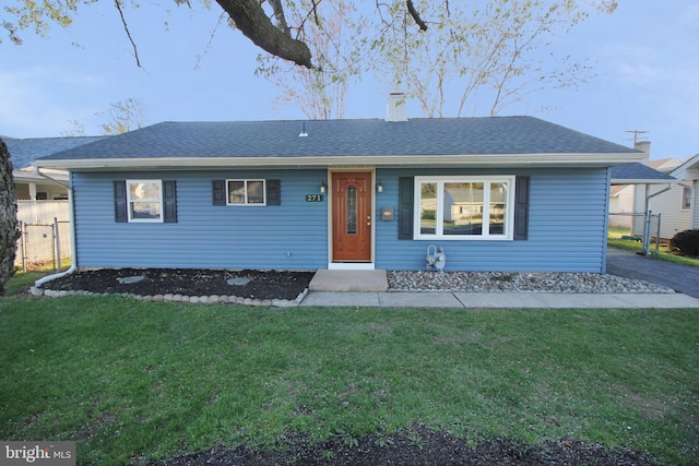 ranch-style home with roof with shingles, fence, a chimney, and a front yard