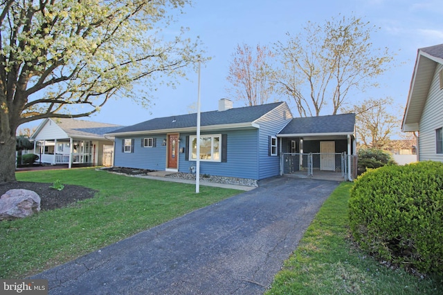 ranch-style home featuring aphalt driveway, a front yard, an attached carport, a chimney, and a gate