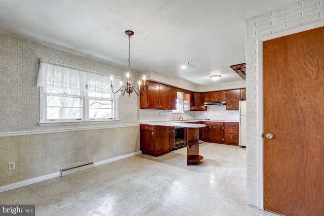 kitchen featuring light countertops, wallpapered walls, freestanding refrigerator, an inviting chandelier, and under cabinet range hood