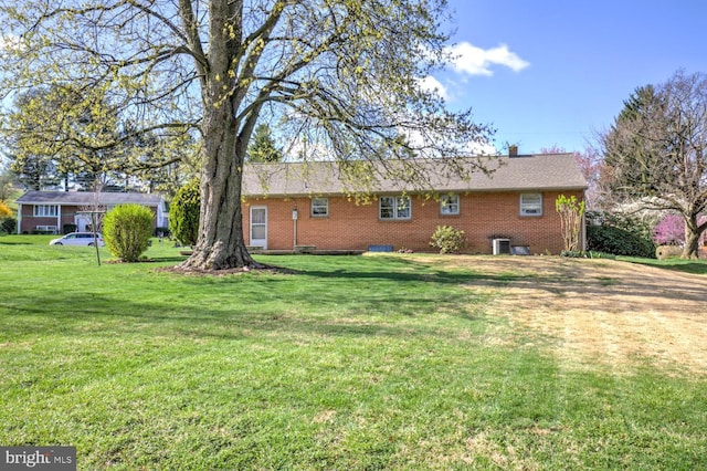 rear view of property featuring brick siding, cooling unit, and a yard