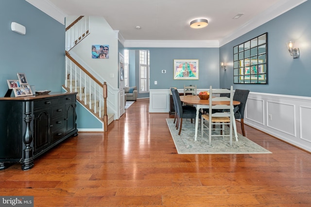 dining space with wood finished floors, stairway, a wainscoted wall, ornamental molding, and a decorative wall