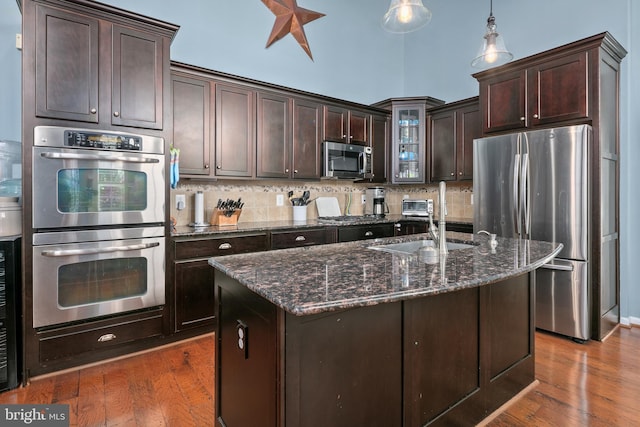kitchen with dark brown cabinetry, a sink, dark stone counters, stainless steel appliances, and backsplash