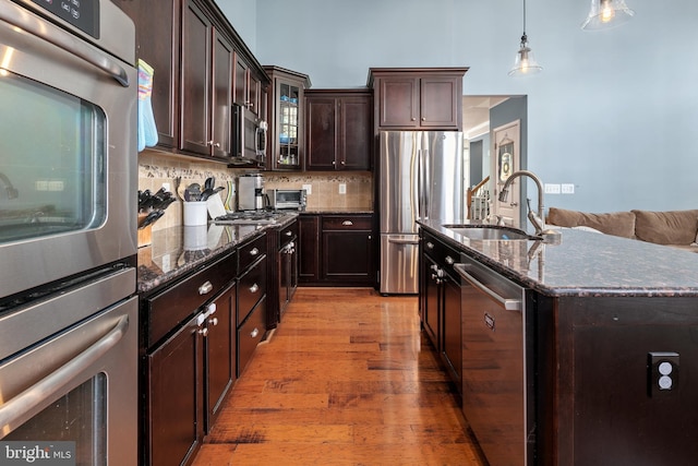 kitchen featuring light wood-style floors, a sink, dark stone counters, and stainless steel appliances