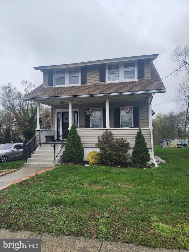 view of front of home with a front yard, roof with shingles, and a porch
