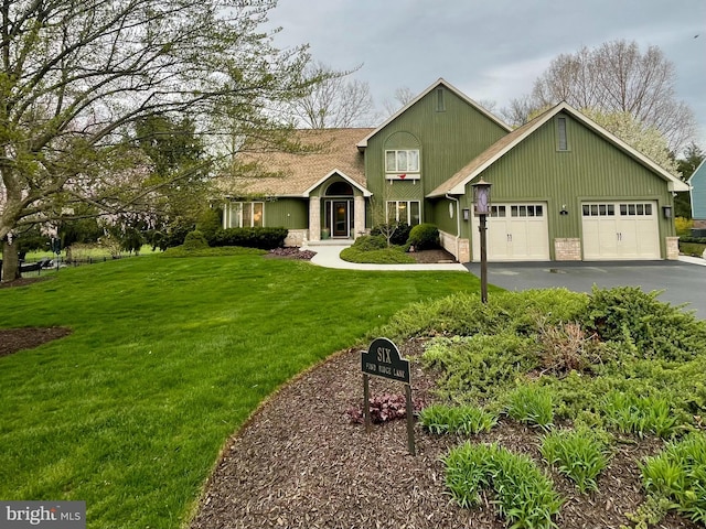 view of front of home featuring stone siding, a garage, a front yard, and aphalt driveway