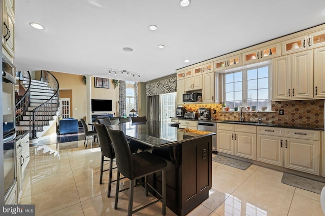 kitchen with a breakfast bar area, light tile patterned floors, a sink, appliances with stainless steel finishes, and backsplash