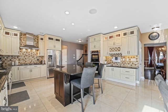 kitchen featuring wall chimney exhaust hood, appliances with stainless steel finishes, cream cabinets, and a breakfast bar