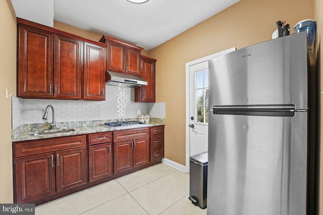 kitchen with backsplash, under cabinet range hood, a sink, reddish brown cabinets, and stainless steel appliances