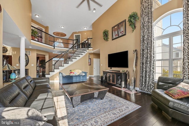 living room featuring a high ceiling, hardwood / wood-style flooring, baseboards, decorative columns, and stairway