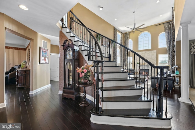 stairway with baseboards, ceiling fan, wood-type flooring, and ornate columns