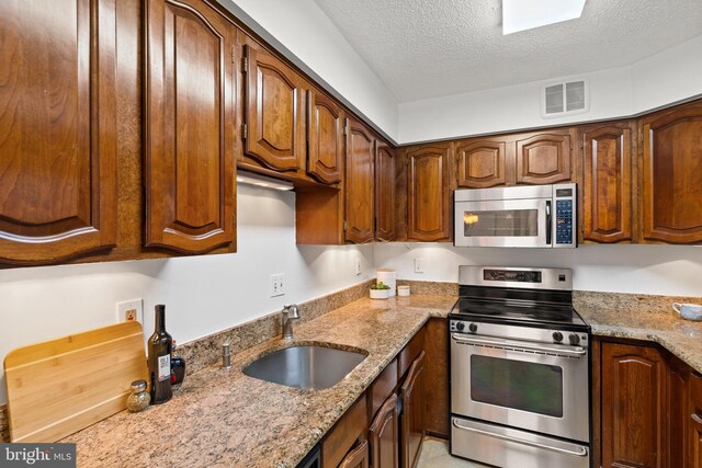 1077 30th St NW Unit 612, Washington, DC 20007 - kitchen featuring stainless steel appliances, a textured ceiling, a sink, and light stone countertops
