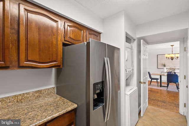 1077 30th St NW Unit 612, Washington, DC 20007 - kitchen featuring stainless steel fridge, a chandelier, estacked washer and dryer, brown cabinetry, and a textured ceiling