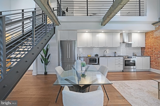 515 N Washington St Unit 404, Alexandria, VA 22314 - kitchen with wall chimney range hood, appliances with stainless steel finishes, white cabinetry, baseboards, and dark wood-style floors