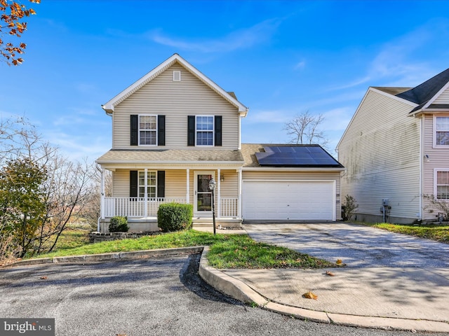 traditional-style house featuring a porch, driveway, solar panels, roof with shingles, and an attached garage