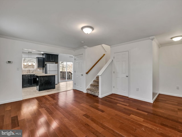 unfurnished living room with crown molding, stairs, baseboards, and hardwood / wood-style floors