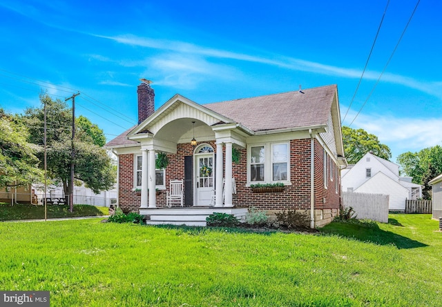 bungalow-style house featuring fence, a chimney, a front yard, and brick siding