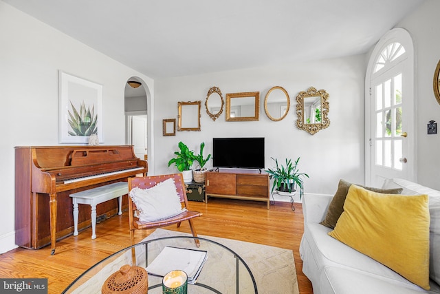 living area with arched walkways, baseboards, and wood finished floors