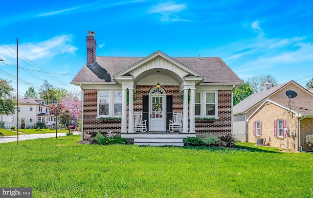 bungalow featuring a porch, brick siding, a chimney, and a front yard