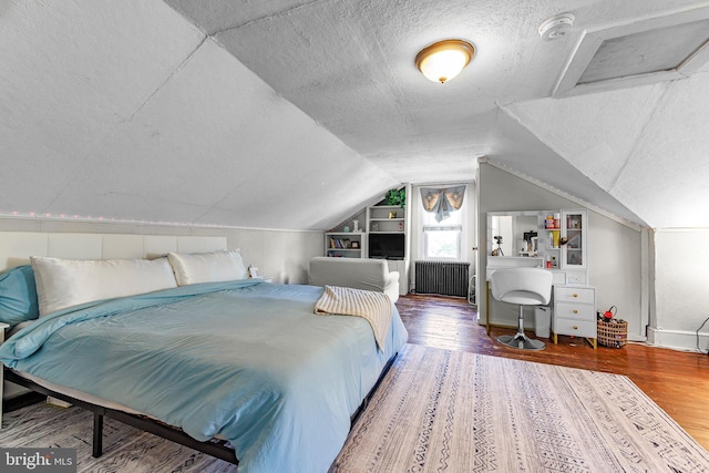 bedroom with wood finished floors, a textured ceiling, radiator heating unit, and vaulted ceiling