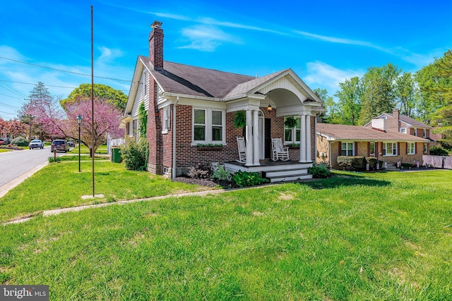 view of front of home with a porch, a front lawn, a chimney, and brick siding